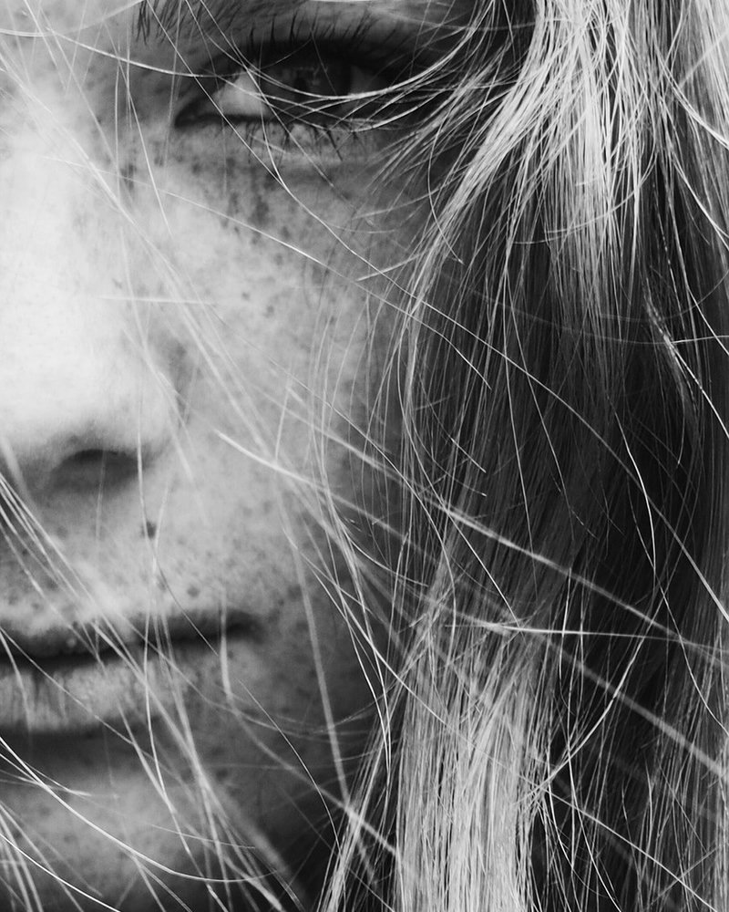 Intimate close-up portrait with freckles and hair across face